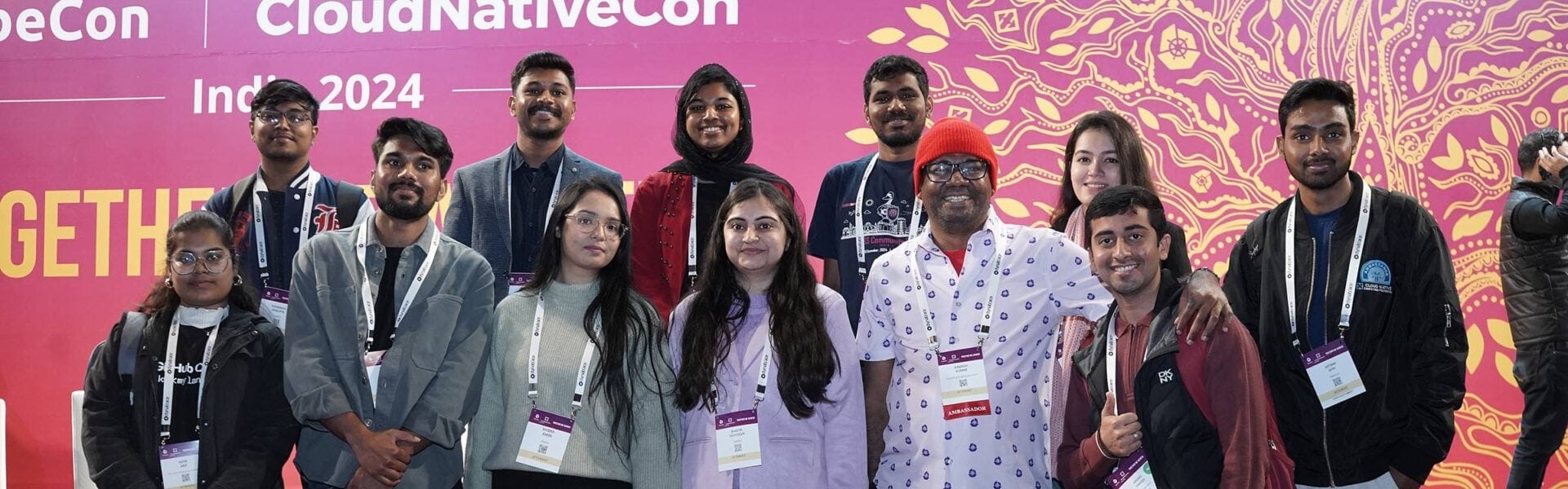 A group photo of 12 attendees in front of the KubeCon + CloudNativeCon sign.