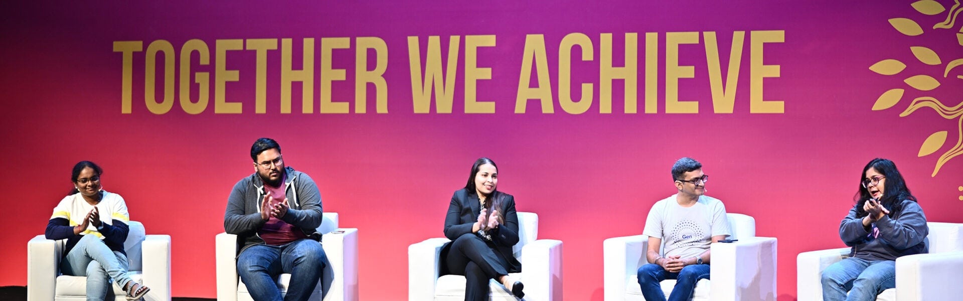 A panel of 5 speakers seated on stage smiling and clapping.