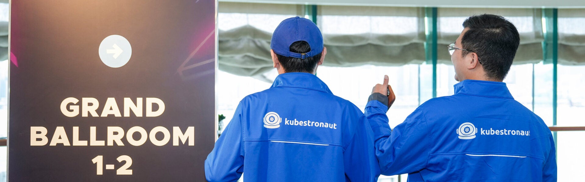 2 men showing the back of their jackets that say "kubestronaut" on them.