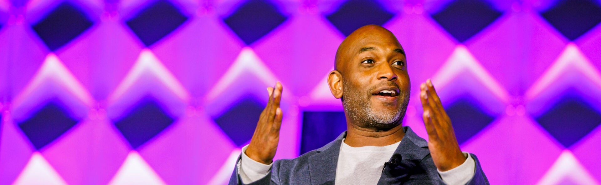 A close up of a man enthusiastically speaking on a bright stage.