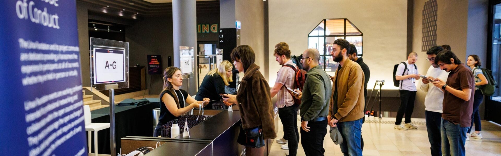 Attendees stand in short lines at the registration desk, receiving badges and assistance from staff members behind the desk.