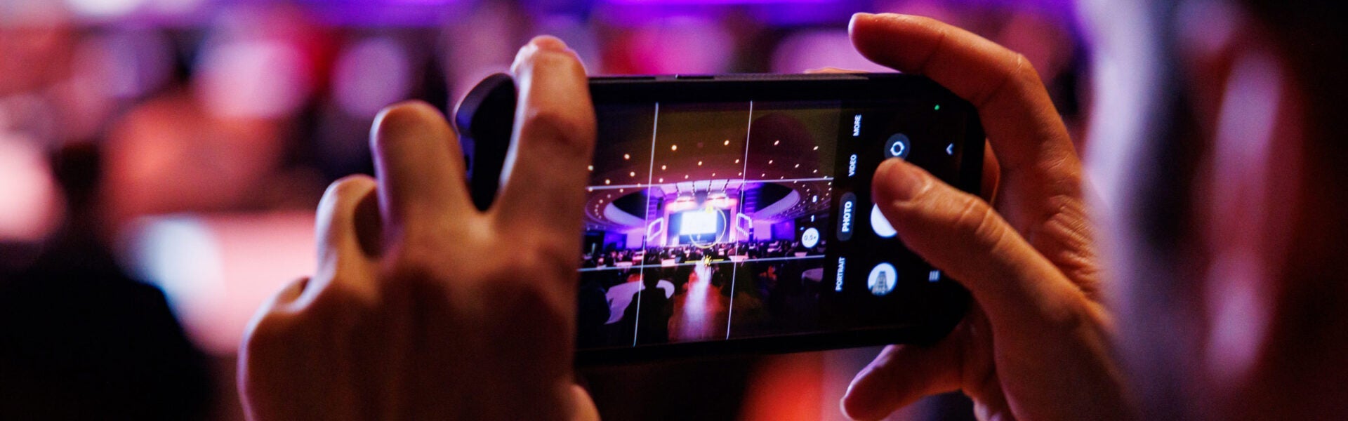 A close-up of someone taking a photo on their phone, with the full stage visible on the phone screen.