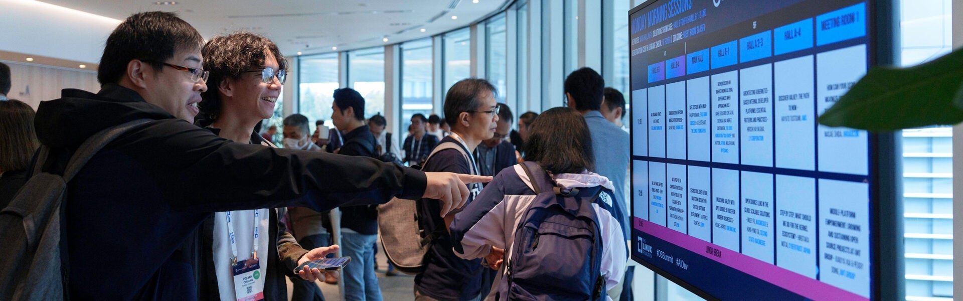 Two attendees smiling and pointing at a schedule on a screen.