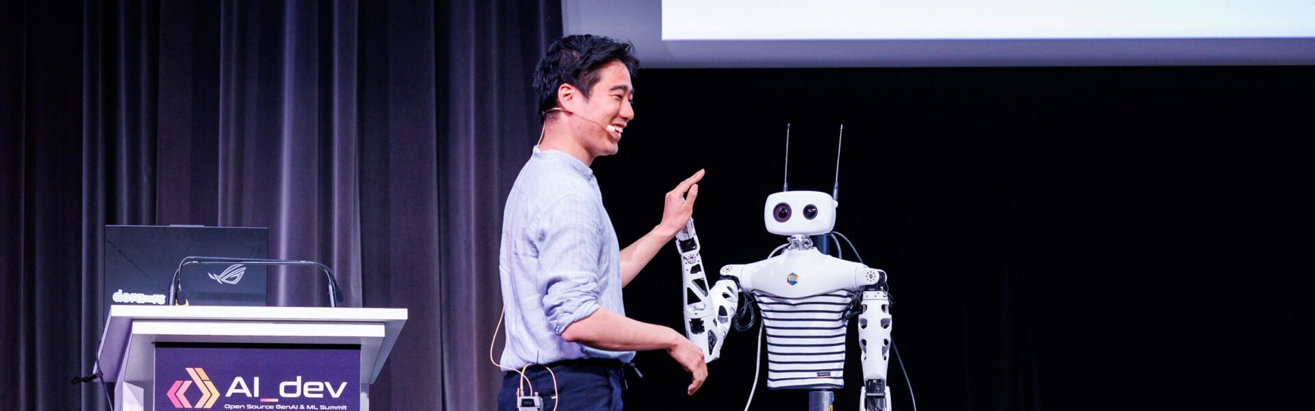 A speaker on stage smiling while high-fiving a robot.