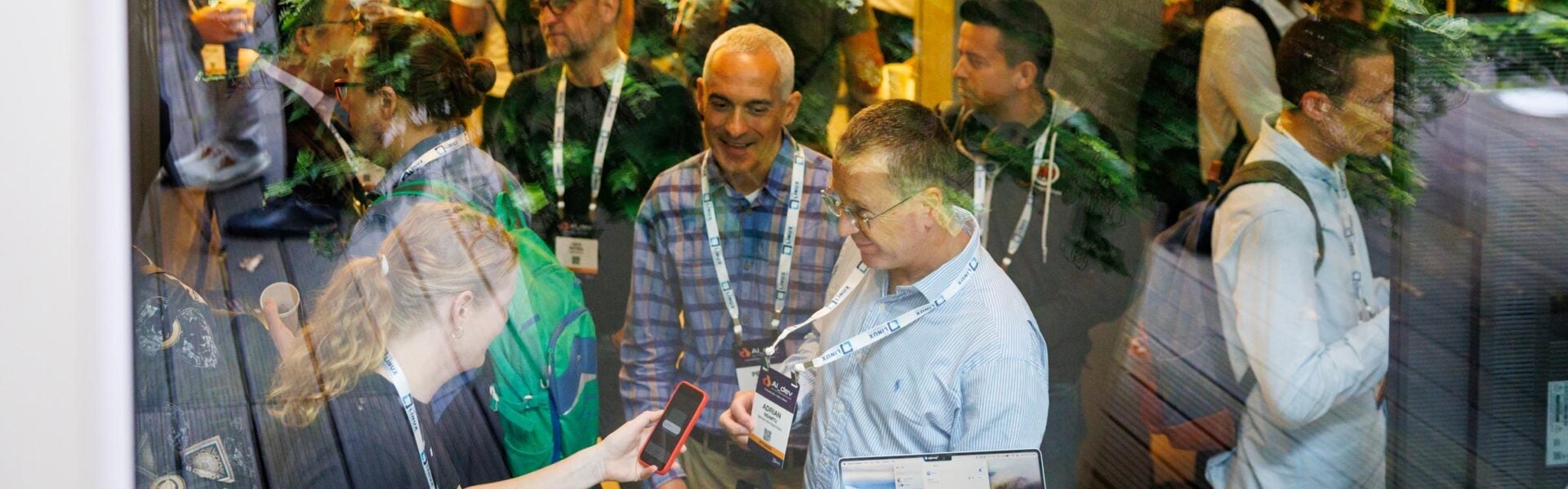 A view through a window of event attendees walking around the space, with one attendee having their badge scanned by a sponsor.