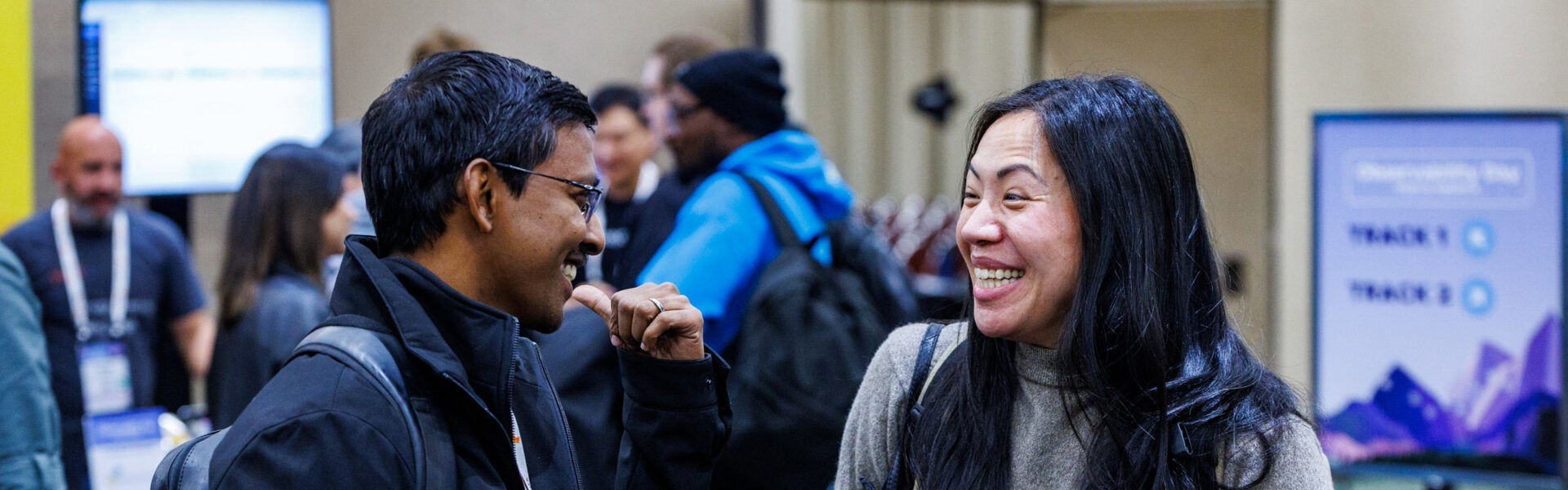 A man & woman talking to each other and laughing with more attendees in the background.