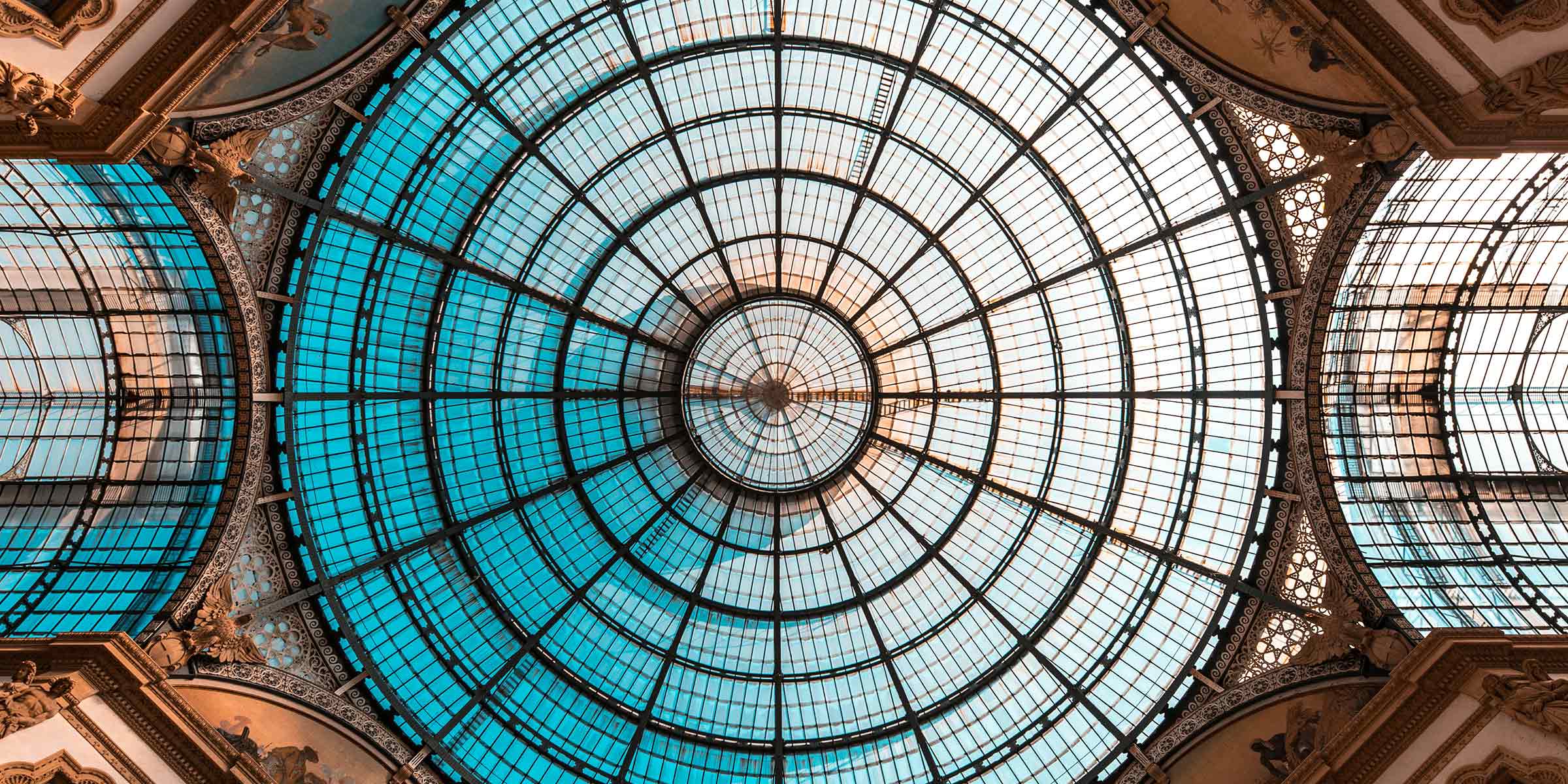 Ground-level view looking up at the ceiling of Galleria Vittorio Emanuele, featuring a large circular window in the center surrounded by additional windows.