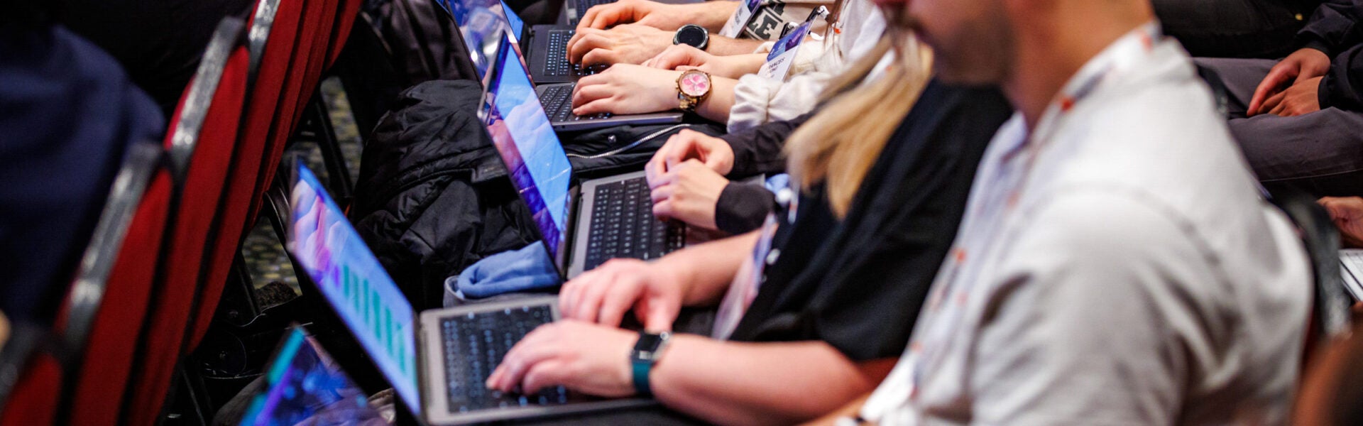 A close up of a row of people with their hands on the keyboards of their laptops.