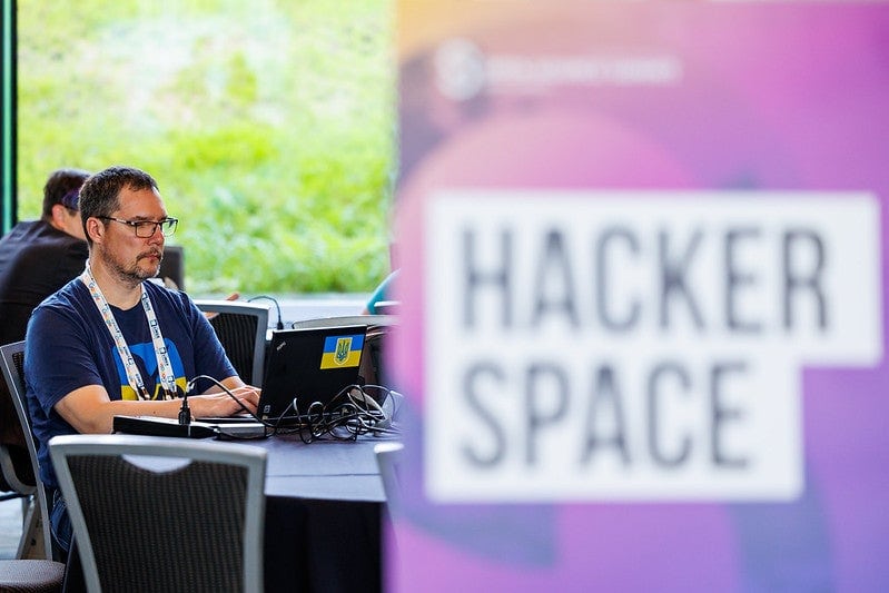A man working on a laptop behind a sign that reads "Hacker Space".