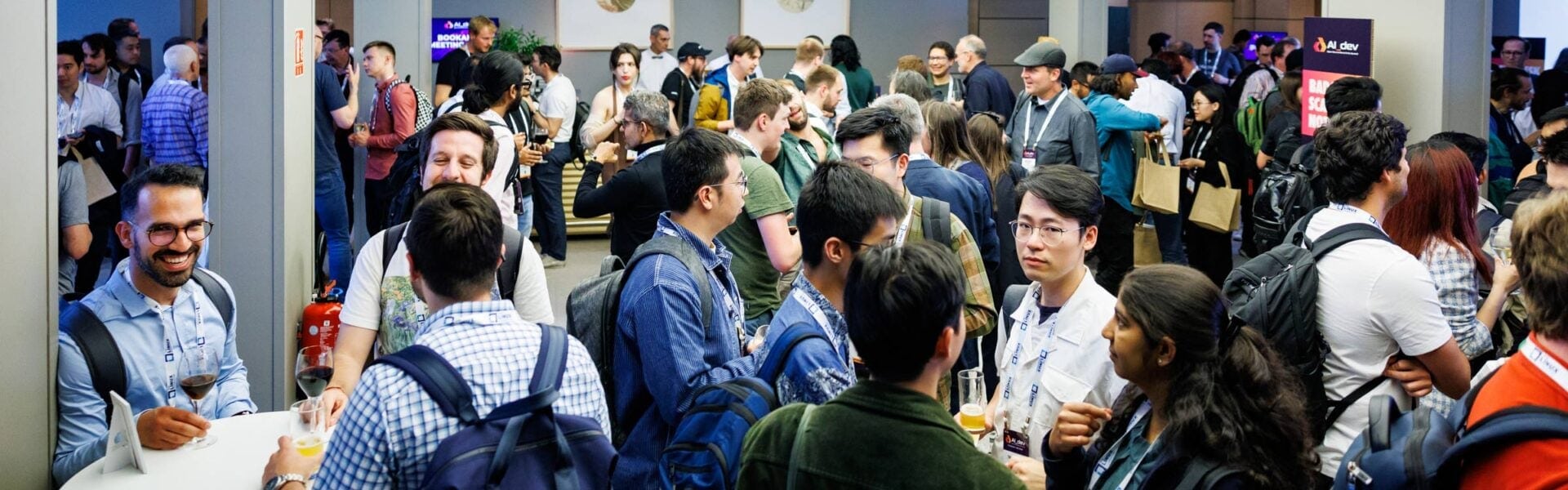 A large group of attendees gathered in a common space enjoying refreshments and having conversations.