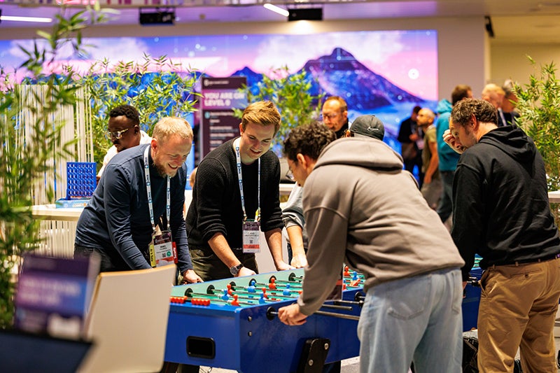 4 people smiling and playing foosball.
