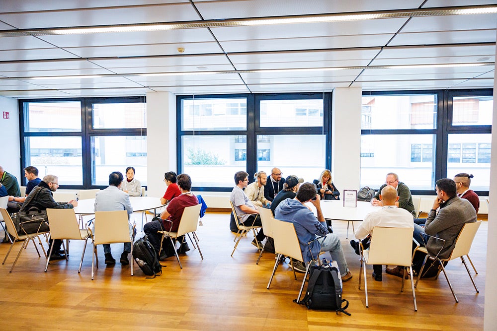 Event attendees seated around white tables having a discussion.
