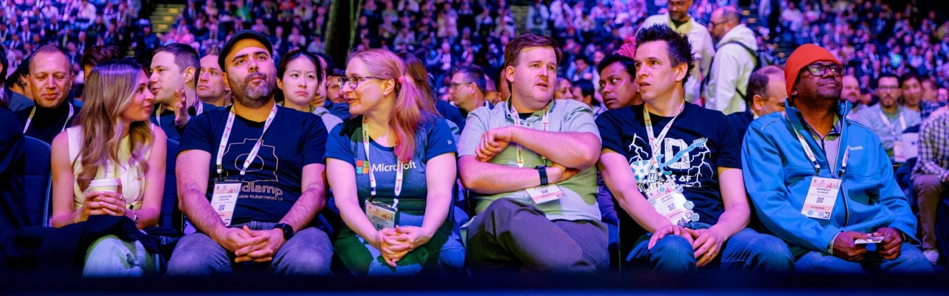 Close-up of attendees seated in a row at an event, some chatting with each other while others look toward the stage.