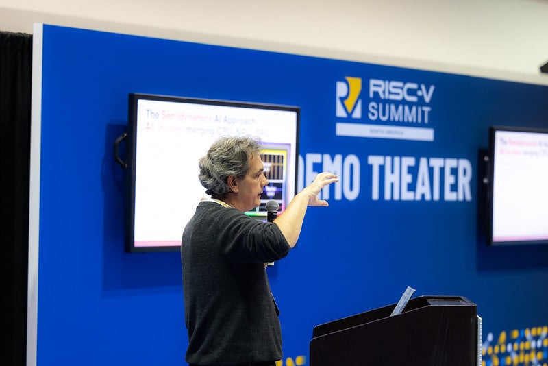 A man standing behind a podium, in front of a sign that reads "Demo Theater".