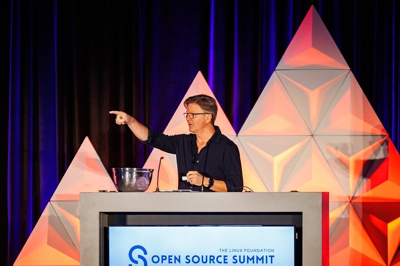 A man standing behind a podium, pointing away from himself.