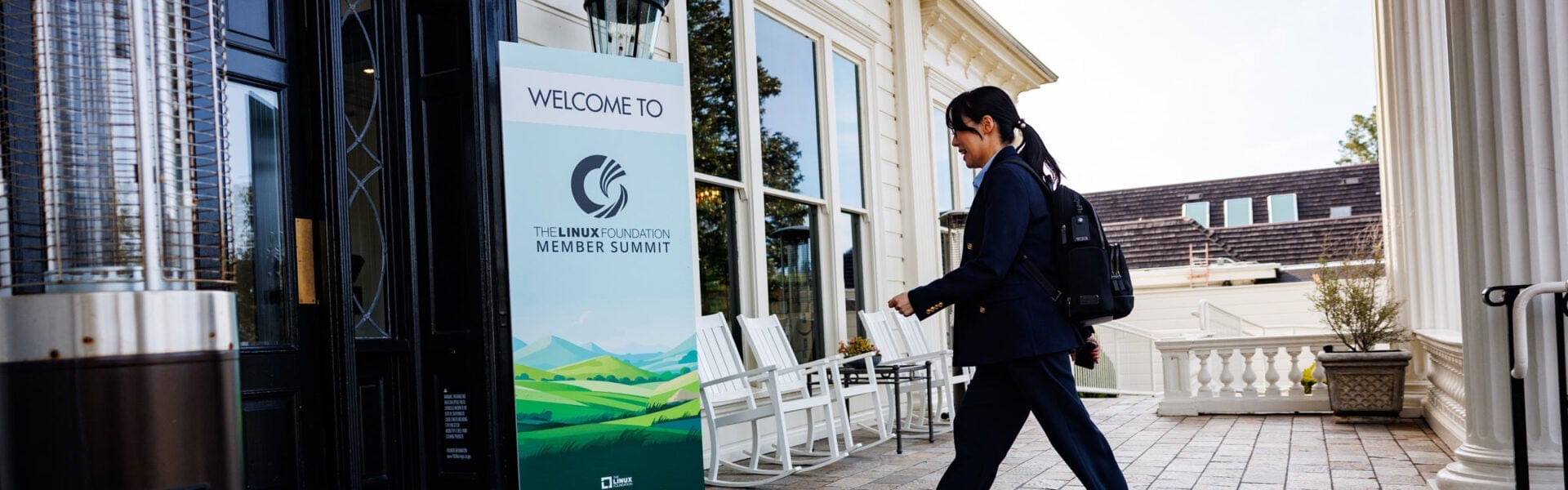 A woman walking towards a door with a sign next to it that says "Welcome to The Linux Foundation Member Summit."