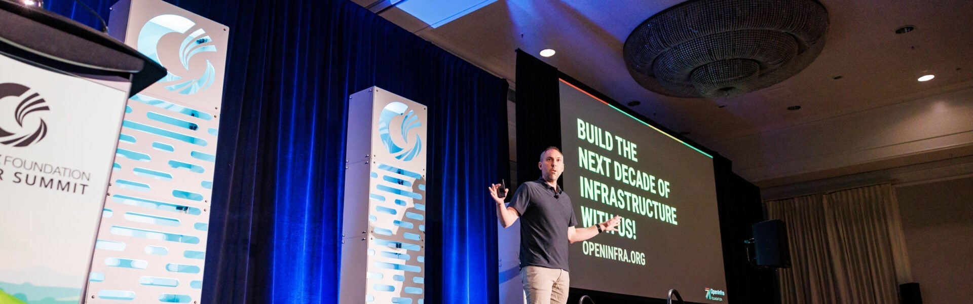 A speaker onstage with a sign behind him that says "Build the next decade of infrastructure with us!"