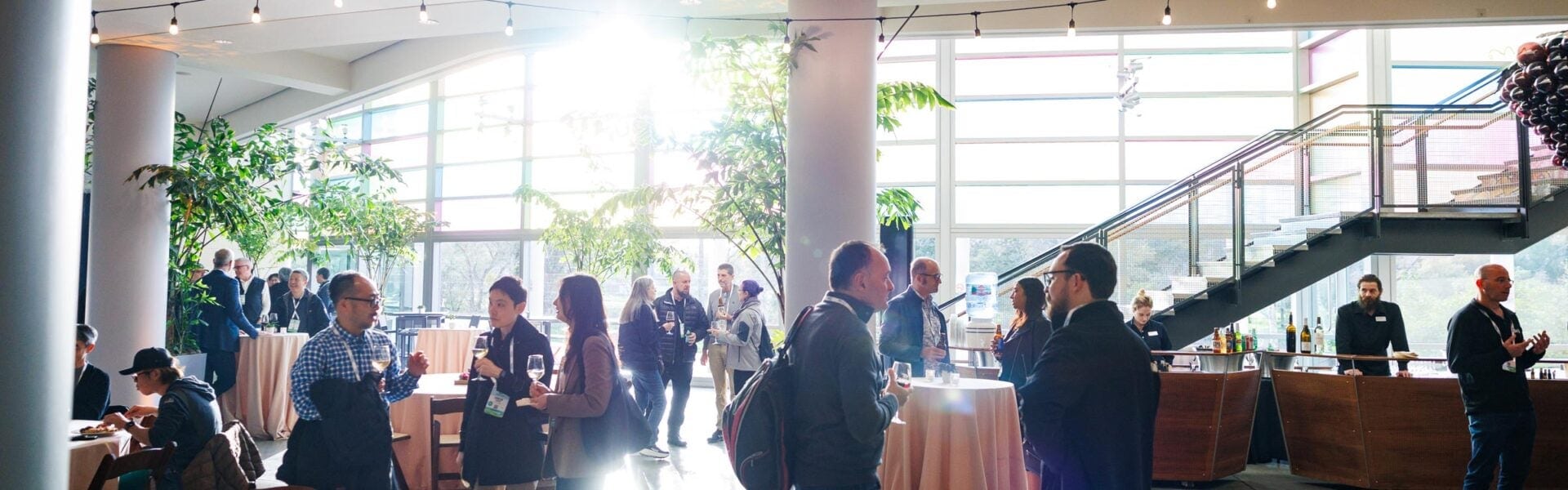 Attendees connect in a sunlit venue with vibrant windows.