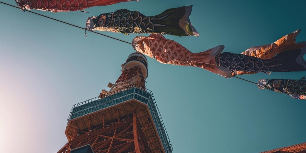Photograph of the Tokyo tower taken from ground level with kites flying overhead.