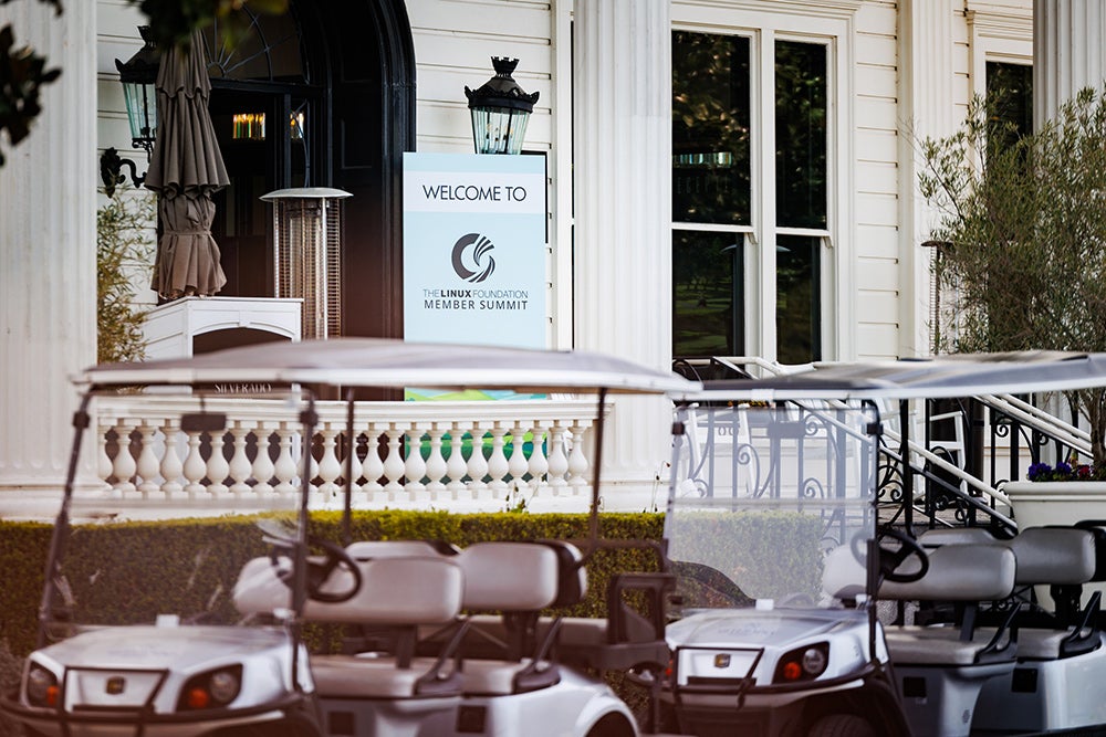 Golf carts parked outside of the venue with a sign near the door that says "Welcome to the Linux Foundation Member Summit."