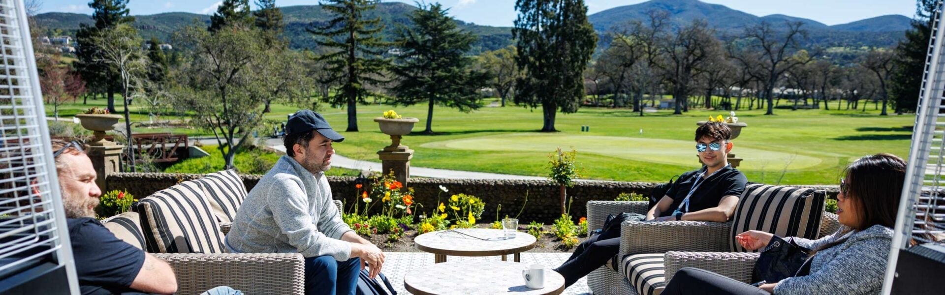 Four attendees sit on a patio with a golf course in the background, chatting in the sun.
