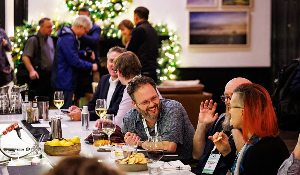 People gathered around a table enjoying refreshments & having conversations.
