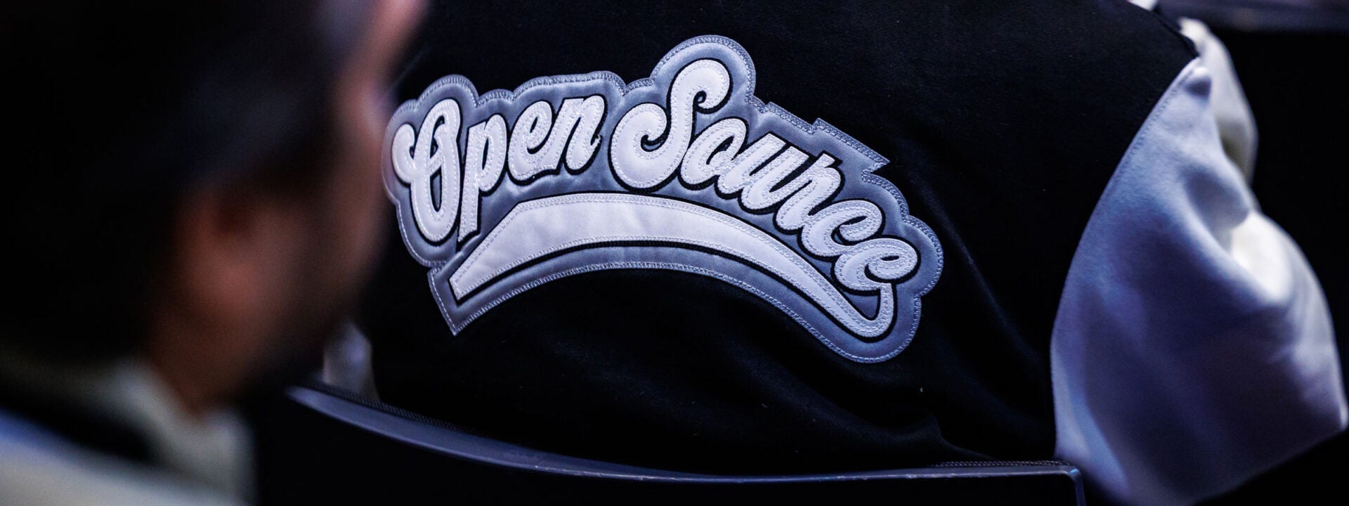 Close-up of a black and white jacket with the words “Open Source” stitched across the back.