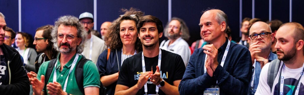 A group of attendees clap and smile while watching a presentation at a conference.