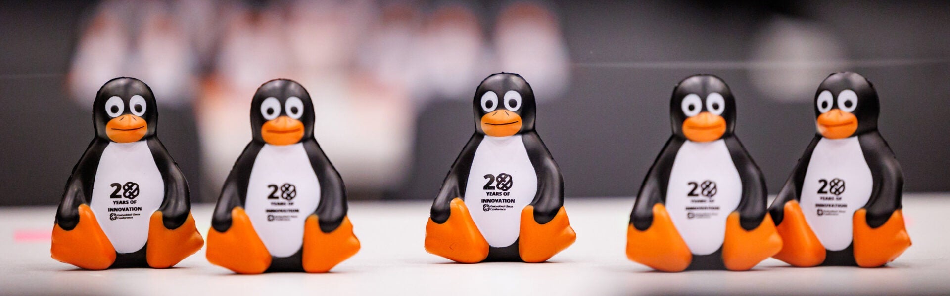 A row of small penguin figurines with “20 Years of Innovation” printed on them displayed on a table.