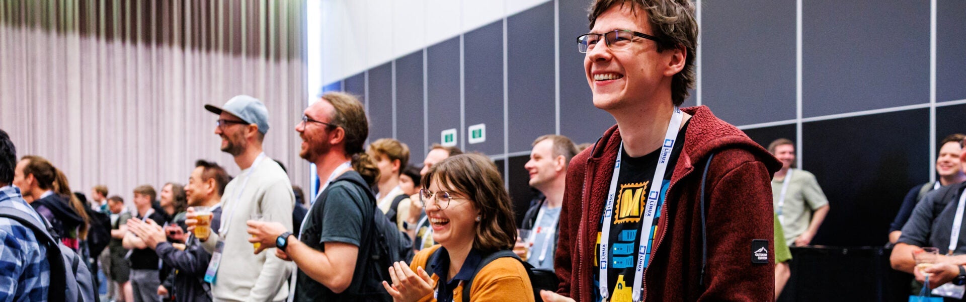 A group of smiling attendees stands together at an event, clapping and enjoying the moment.