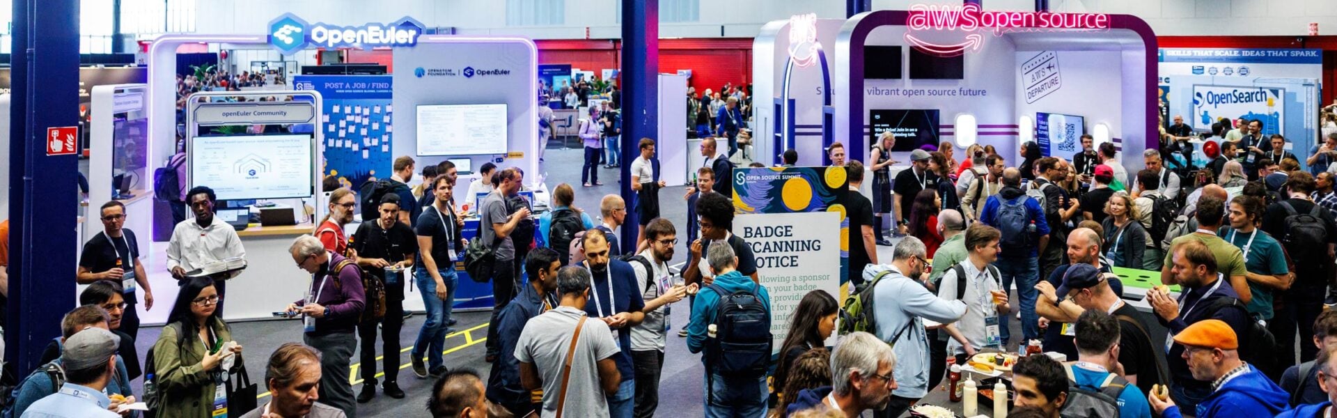 Attendees network and visit sponsor booths in a busy expo hall at Open Source Summit, with displays from open source organizations and companies in the background.