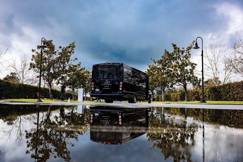 A shuttle van and it's reflection in a puddle on the ground.