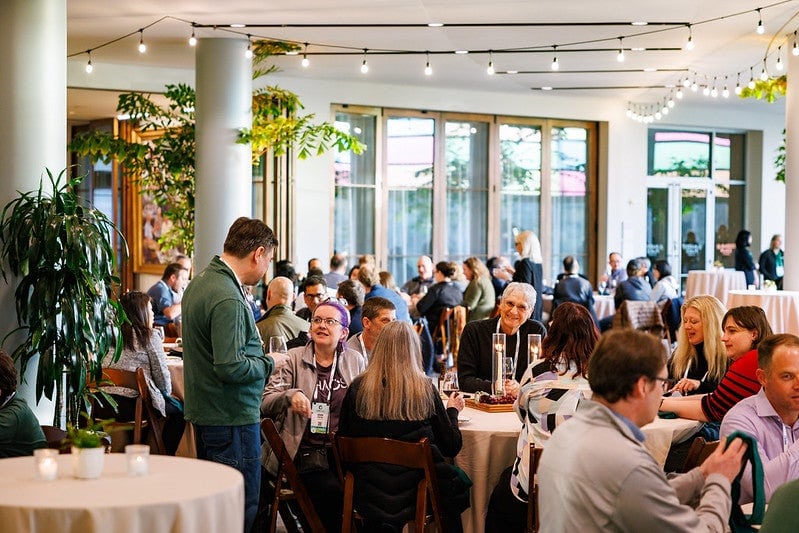 A room filled with people seated at round tables speaking.