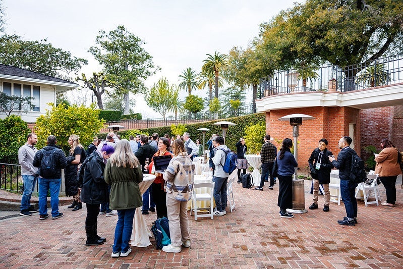A group of attendees standing on a patio drinking and talking with one another.