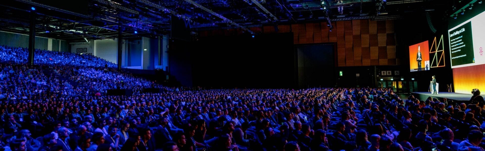 A full auditorium of attendees listening to a speaker on stage.