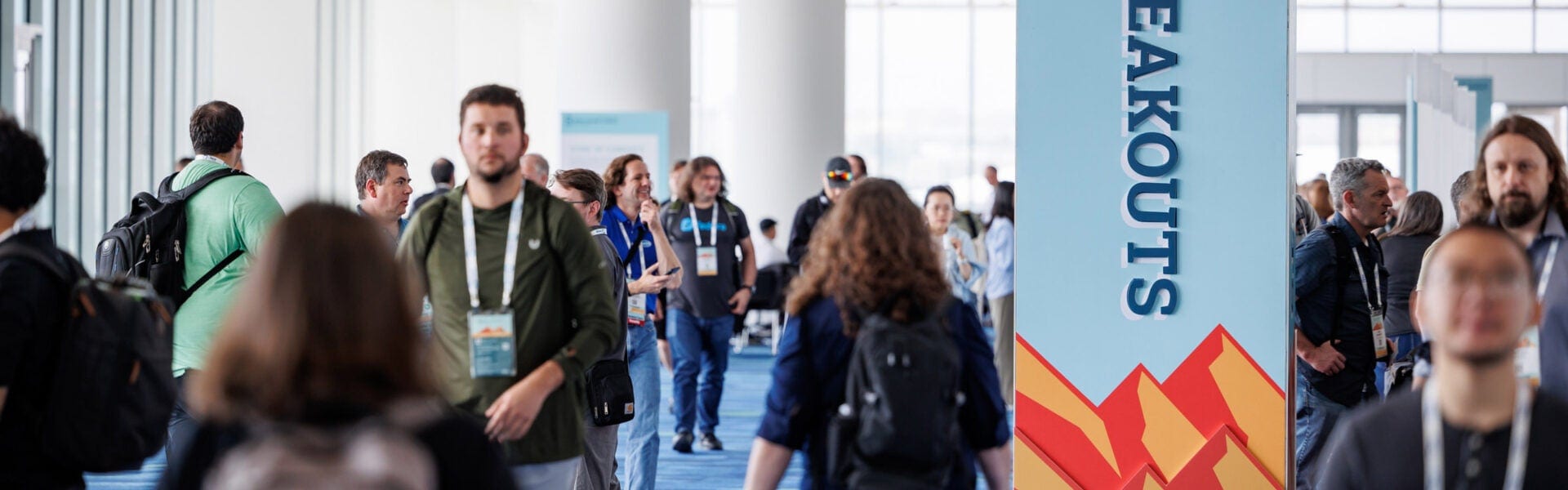 Attendees walk through a bright conference hallway past a tall “Breakouts” sign, heading toward sessions.