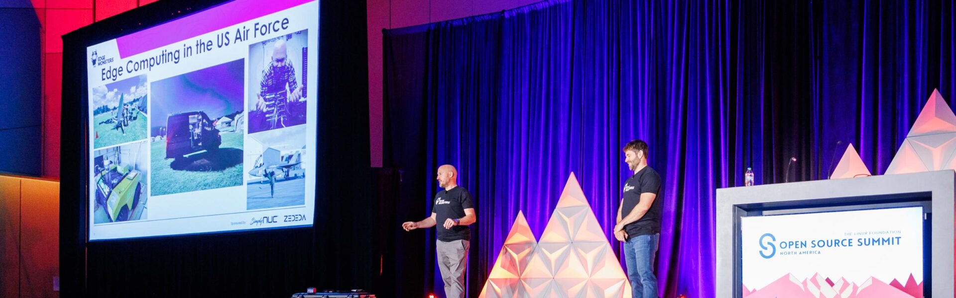 Two speakers stand on stage at the Open Source Summit, giving a presentation titled “Edge Computing in the US Air Force,” with slides showing images of aircraft and technology equipment.