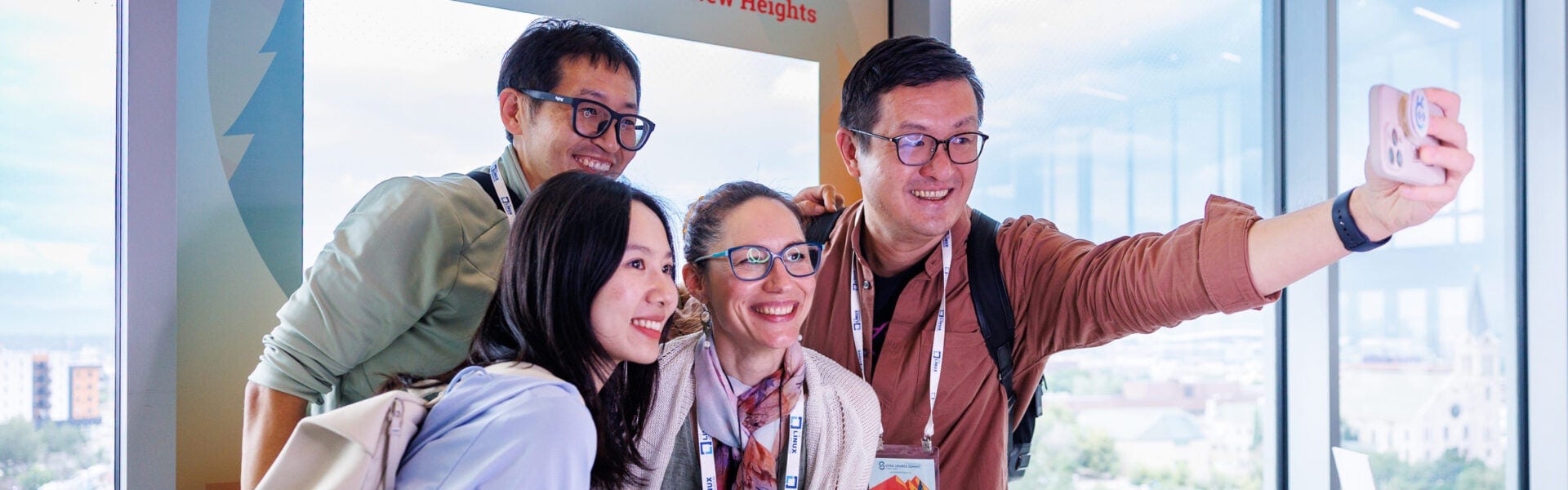 Four attendees gather by a large window to take a selfie, smiling and posing together.