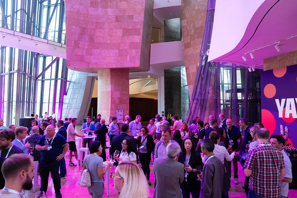 Guests mingle and network over drinks in a brightly lit modern venue with colorful pink lighting.
