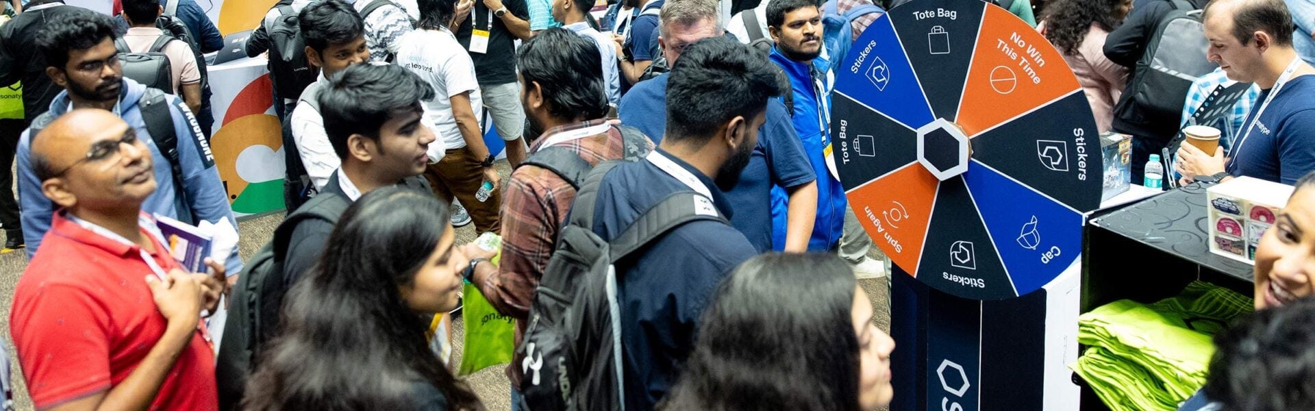 Attendees gathered around a colorful prize wheel at a sponsor booth, engaging with exhibitors at a tech conference.