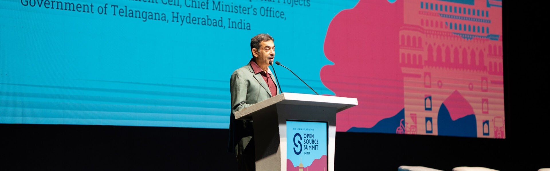 Speaker delivering a keynote from a podium on stage at Open Source Summit India with colorful backdrop behind him