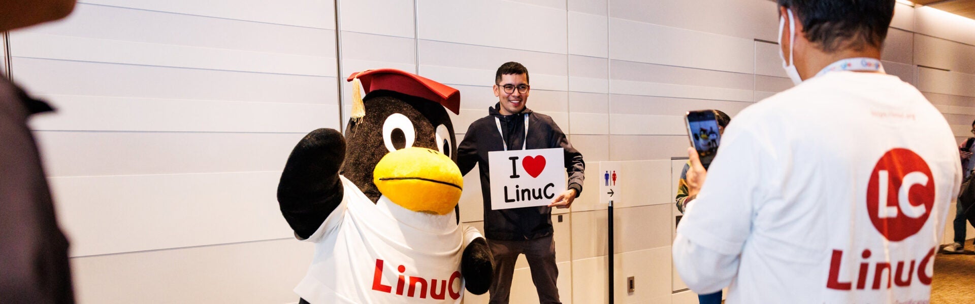 Attendee posing with a Linux penguin mascot holding an “I love LinuC” sign.