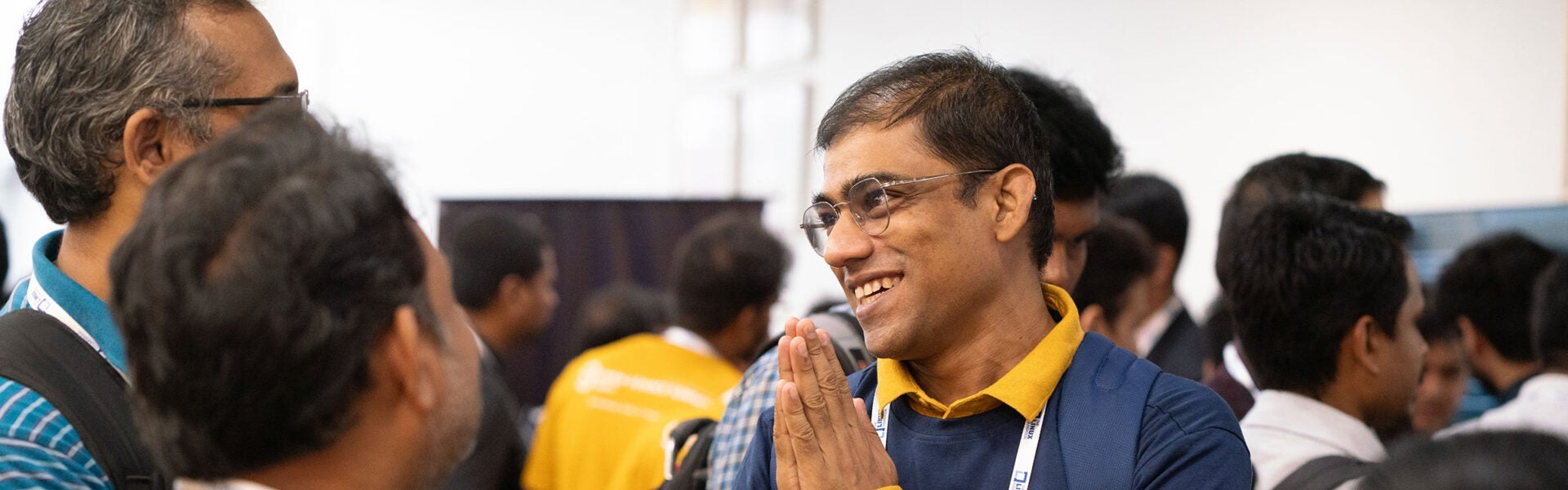 Smiling attendee greeting another participant with hands pressed together in a crowded conference hall