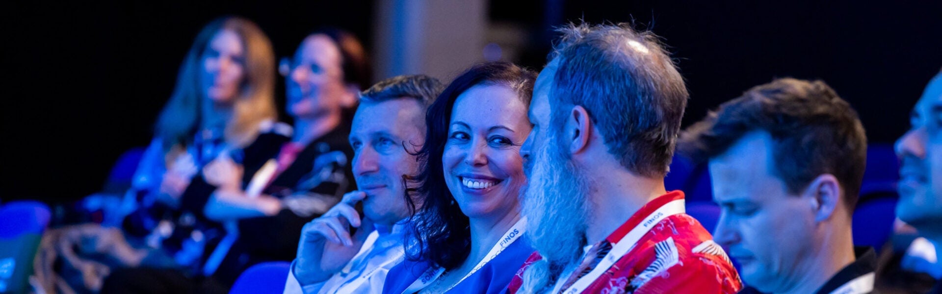Attendees sitting in an audience, smiling and talking with each other during a conference session.