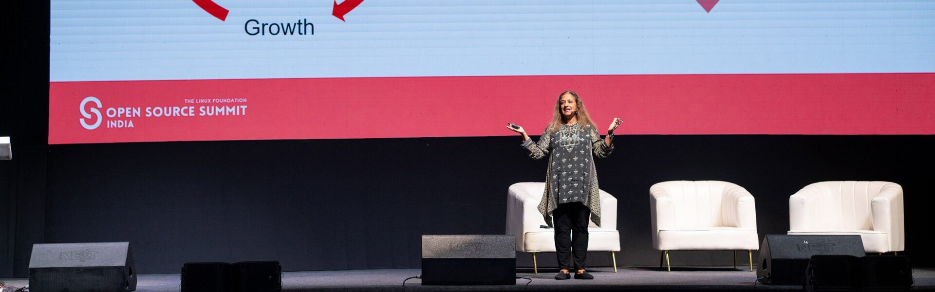 Speaker presenting on stage at Open Source Summit India with event branding visible on large screen behind them