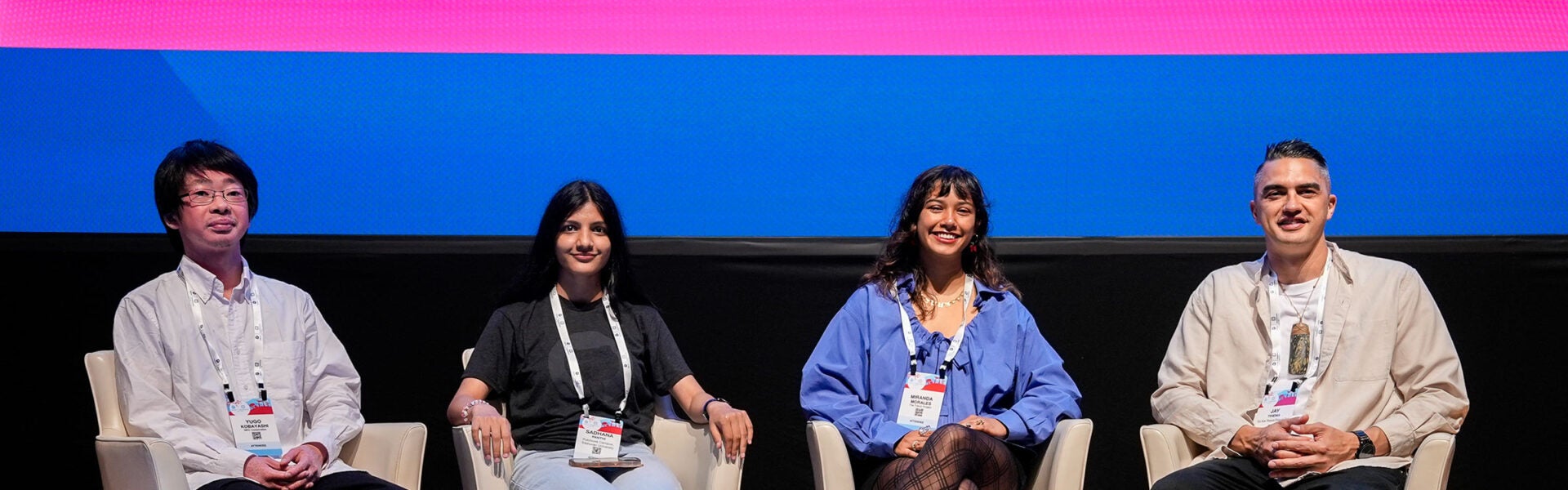 Four panelists sit onstage in front of a colorful screen, smiling toward the audience.
