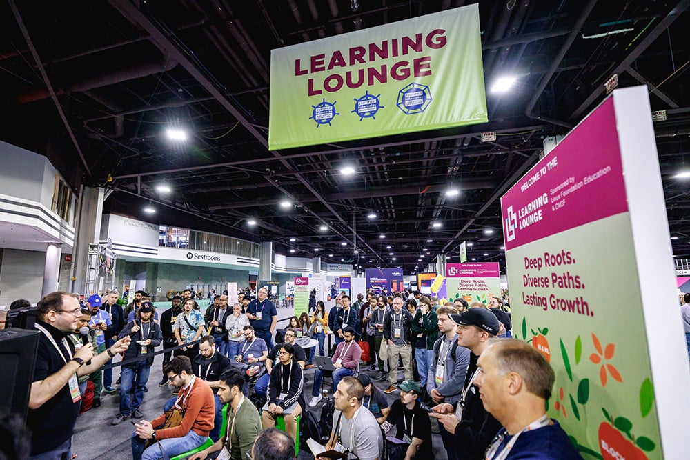 Conference attendees gathered in a Learning Lounge area listening to a speaker beneath a large overhead sign.