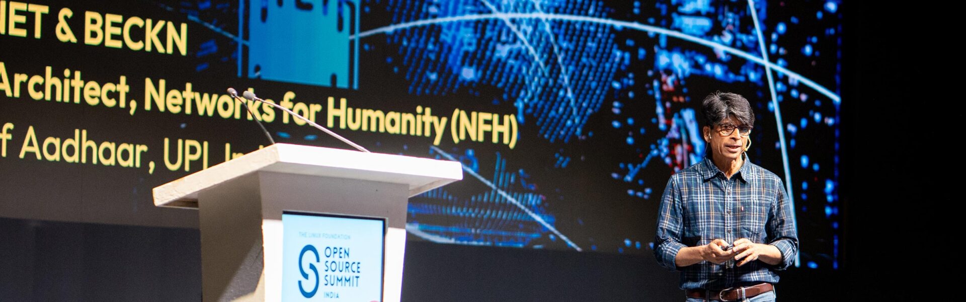 A speaker presents on stage at Open Source Summit India with a digital graphic behind him.