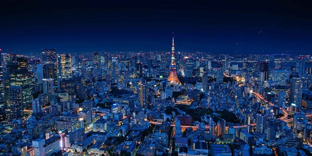 Nighttime aerial view of Tokyo’s cityscape with Tokyo Tower glowing orange among illuminated skyscrapers.