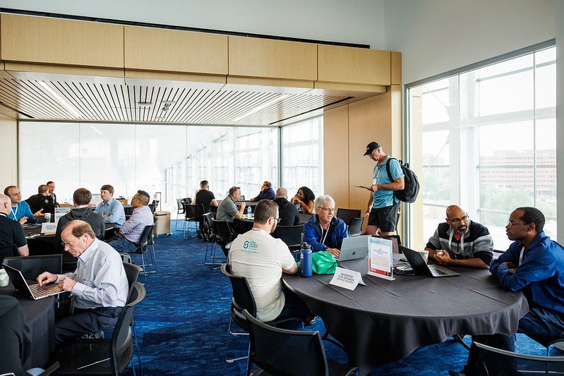 A room filled with round tables with attendees seated and having discussions.
